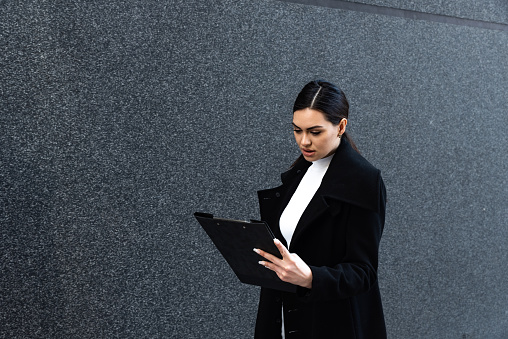 Young female defense attorney or prosecutor reads and checks the case as she walks toward the courtroom where she represents the client. Woman lawyer outdoor