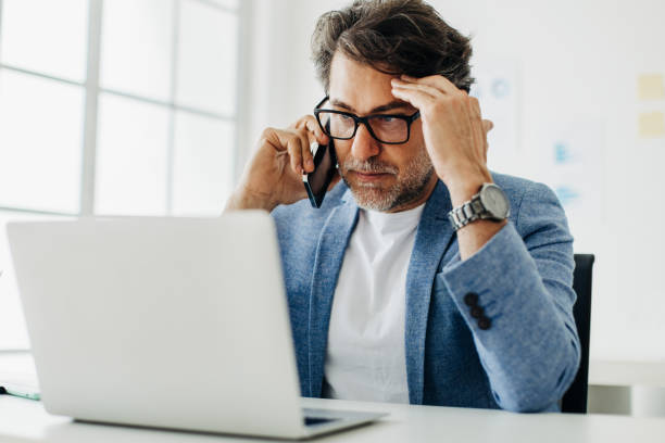 uomo d'affari frustrato che ha una telefonata alla scrivania del suo ufficio - computer old men laptop foto e immagini stock