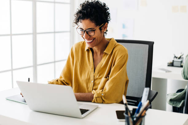 grafikdesignerin lächelt, während sie in einem büro an einem laptop arbeitet - computer women office business stock-fotos und bilder