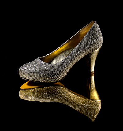 Glittering women heeled shoe on a black background along with reflection on the floor