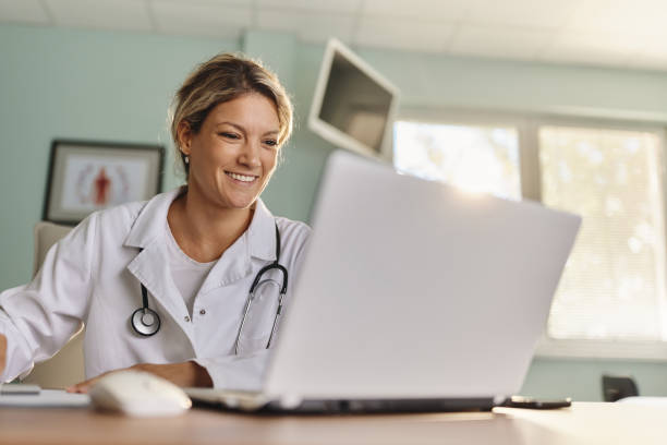 Happy female doctor working on laptop in the office. stock photo
