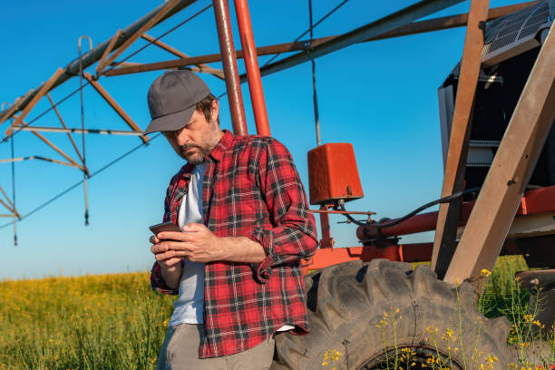 istock Farmer using mobile smart phone next to the center pivot irrigation equipment in rapeseed field 1448477613