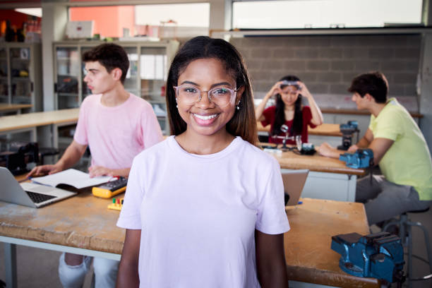 Portrait of a girl standing in a technology class looking at the camera. Vocational training students in the classroom studying electronics, robotics, electricity or some kind of technical college stock photo
