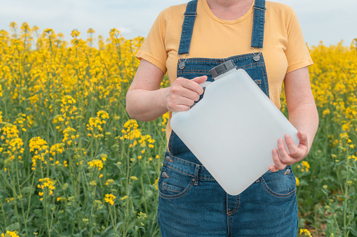 Rapeseed crop protection concept, female farmer agronomist holding jerry can bottle container with pesticide, selective focus