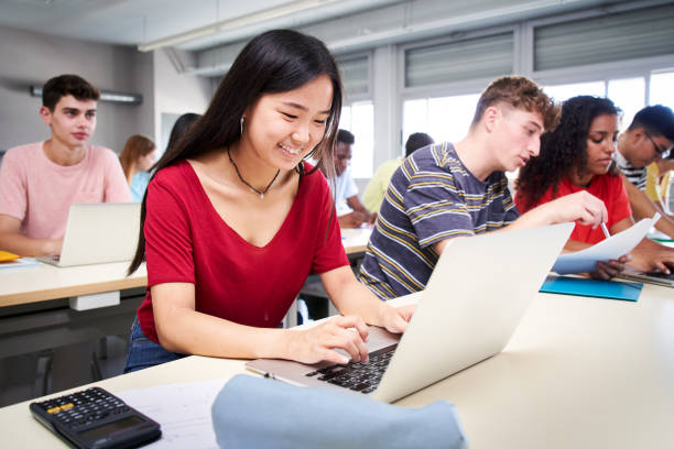 istock Cheerful Smiling Asian high school student girl using a laptop computer at class. A group of happy classmates in classroom. Education and technology 1448478126