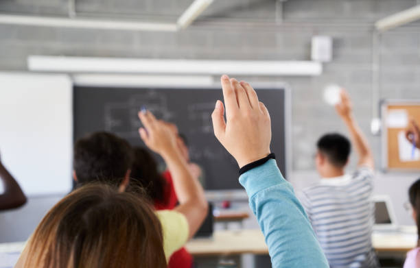 istock Rear view of a student in the classroom raising her hand to ask a question during class. A female high school student asks the teacher a question. Selective focus. 1448478195