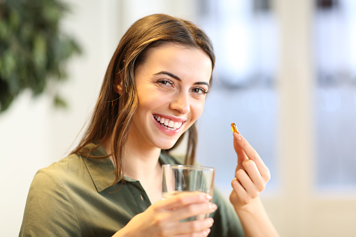 Happy woman showing vitamin pill at home