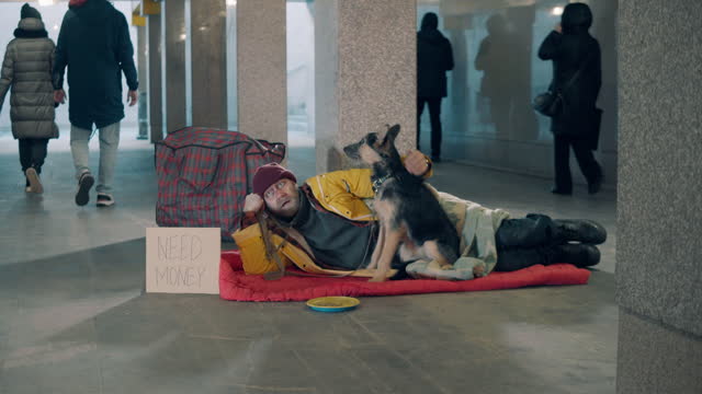 An almsman is lying in the underpass with his dog near him