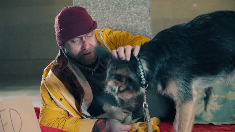 A homeless man is feeding his dog out of his hand