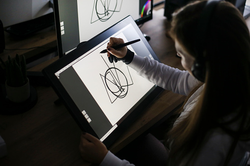 Young woman working at home as a freelance designer, drawing on a pen tablet. About 30 years old, Caucasian female.