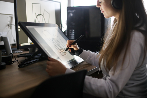 Young woman working at home as a freelance designer, drawing on a pen tablet. About 30 years old, Caucasian female.