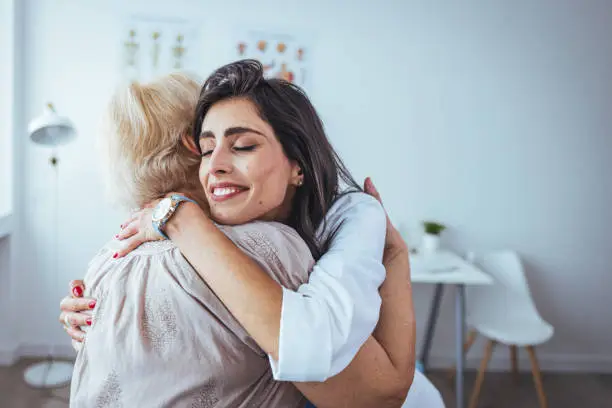 Shot of a young nurse comforting an elderly woman in a retirement home. Shot of a young woman hugging her doctor during a consultation. Caring young medical doctor hugging patient.