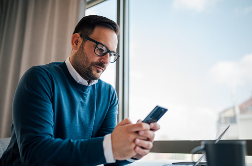 Professional adult businessman, writing a message to his client, from his mobile, at work.