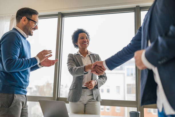 Diverse company employees, happy after a successful meeting. Smiling african american woman, handshaking with her colleague, while her male coworker claps. customer retention stock pictures, royalty-free photos & images