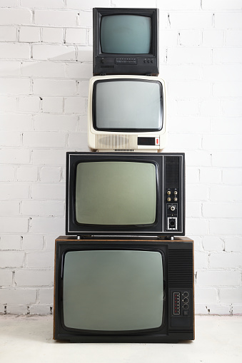 Four old TVs stand against a background of white brick.