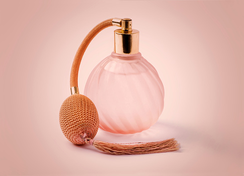 Elegant transparent vintage bottle of perfume with pump and tassel against pink background in studio