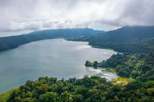 North of Bali. Lake Bratan surrounded with mountains covered with rainforest in rain clouds and fog.
