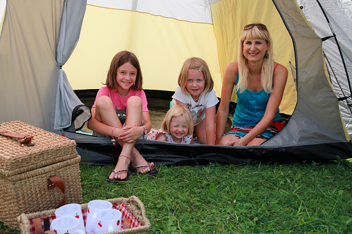 Mother and three girls in a tent camping. Drinking tea, picnic basket and having a good time.