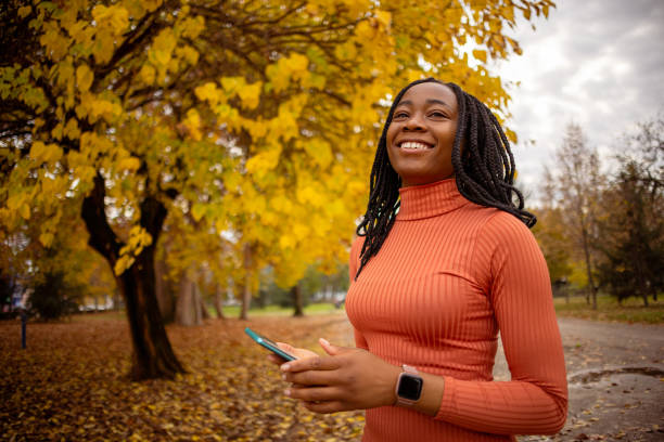 Portrait of woman of Black ethnicity with mobile phone at the public park during autumn day