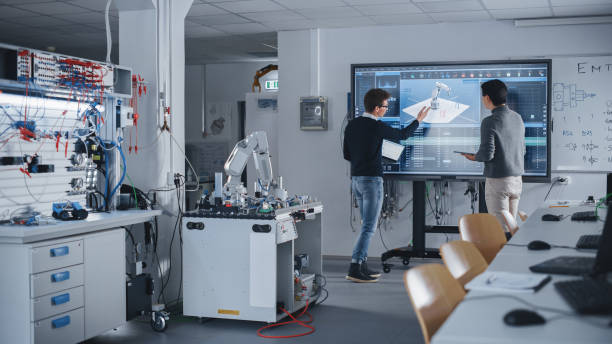 istock Diverse Team of Two Students Standing Near Big Screen with Tablet and Laptop While Discussing Programming and Technologies. Education and Studying in Modern University of Technology Concept. 1448502022