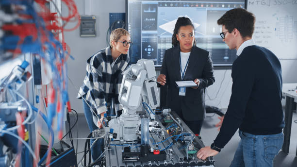 istock In Robotics Development Laboratory: Black Female Teacher and Two Students Work With Prototype of Robotic Hand. Young Student Telling Something with Smile and Brainstorming with Her Team. 1448502084