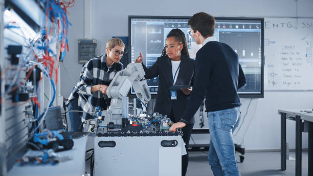 nel laboratorio di sviluppo della robotica: insegnante donna nera e due studenti lavorano con il prototipo della mano robotica. giovane studentessa che racconta qualcosa con il sorriso e il brainstorming con il suo team. - teacher professor science university foto e immagini stock