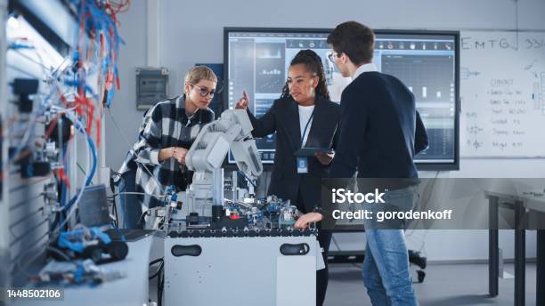 In Robotics Development Laboratory Black Female Teacher And Two Students Work With Prototype Of Robotic Hand Young Student Telling Something With Smile And Brainstorming With Her Team Stock Photo - Download Image Now