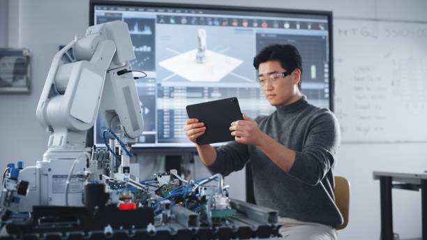 istock Student Holding Tablet and Controlling Robot Hand Moving at Different Ways At University Class. Asian Man Developing Software Production for Robotics Facility. Computer Science Concept. Close Up View 1448503239