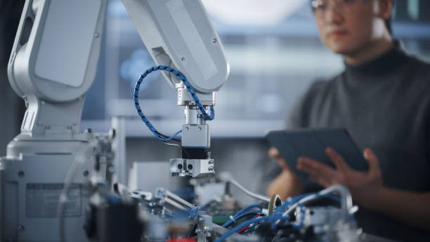 istock Student Holding Tablet and Controlling Robot Hand Moving at Different Ways At University Class. Asian Man Developing Software Production for Robotics Facility. Computer Science Concept. Close Up View 1448503258