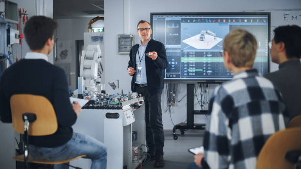 istock Teacher Holding Microchip for Futuristic Equipment During the Lesson while Robotic Arm Moving Nearby. Diverse Group of Young Engineers Sitting at University. Computer Science Education Concept 1448503826