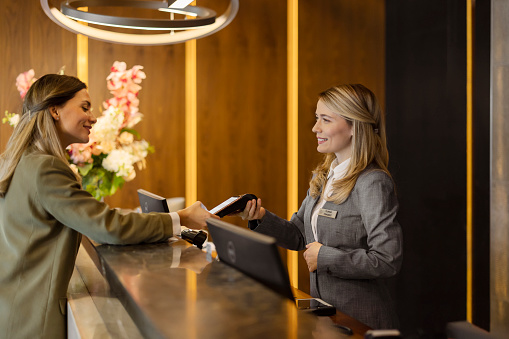 Cheerful receptionist standing at the front desk of a co-working space. Friendly female assistant looking at the camera while working at the reception in a modern office.