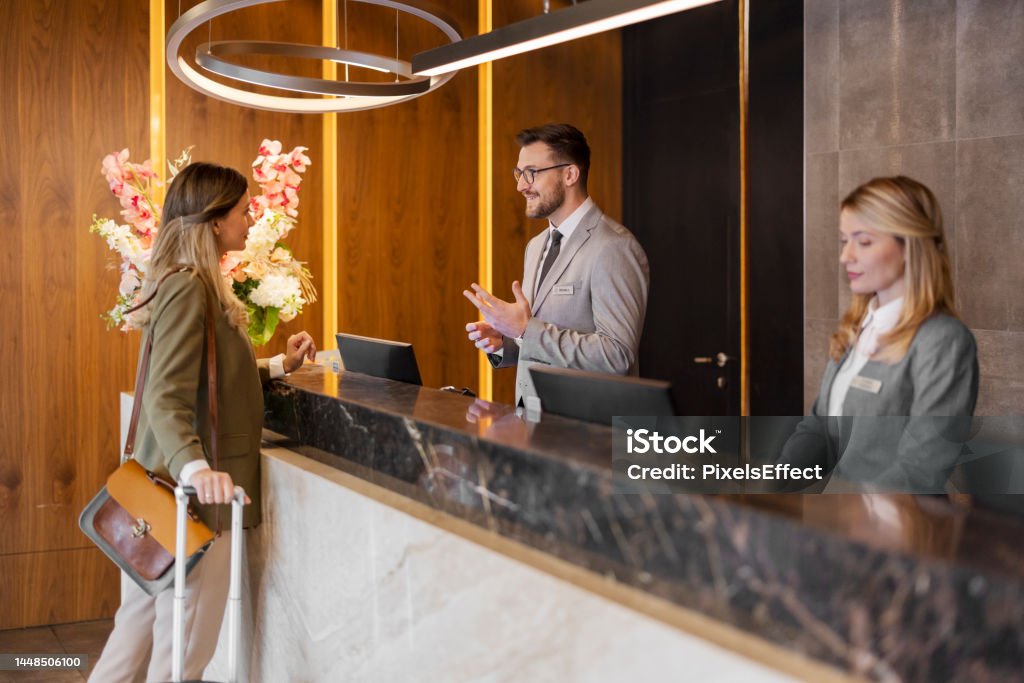 Male hotel receptionist assisting female guest Positive bearded young receptionist standing at the desk and talking with the friendly visitor Hotel Stock Photo