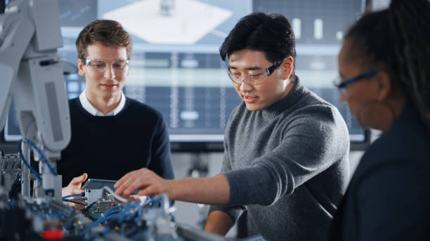istock Male Student Holding a Tablet And Pointing at Robotic Hand While Working on Project with Asian Classmate and Black Teacher. Modern Technologies, Science and Developing at University Concept. 1448507494