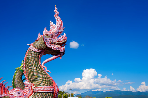 Side view of colorful traditional serpent statues on bannister of Thai temple against cloud on blue sky with beautiful rural scene background