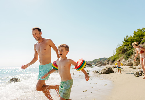 Happy family having fun on sandy beach near sea at sunset