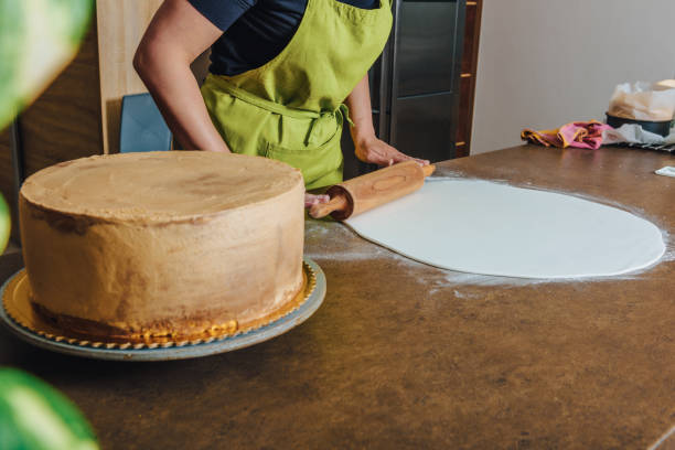 istock Woman using rolling pin preparing pink fondant for cake decorating, hands detail. DIY, sequence, step by step, part of series. 1448513608