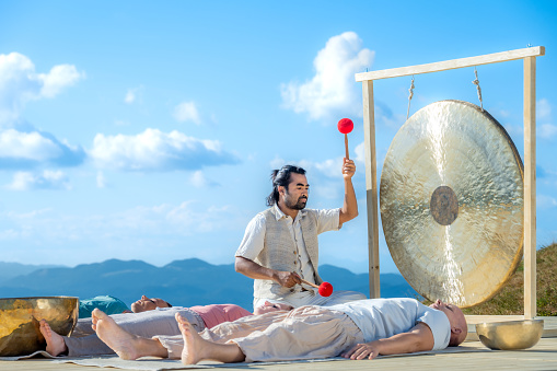 Male therapist playing gong while performing music therapy during sunny day.