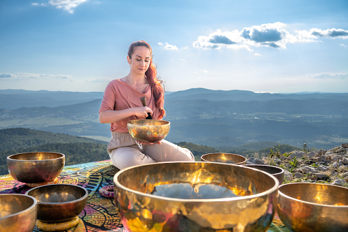 Young woman therapist playing rin gong against mountain during sunny day.