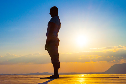 Side view of man practising yoga on deck during sunset.