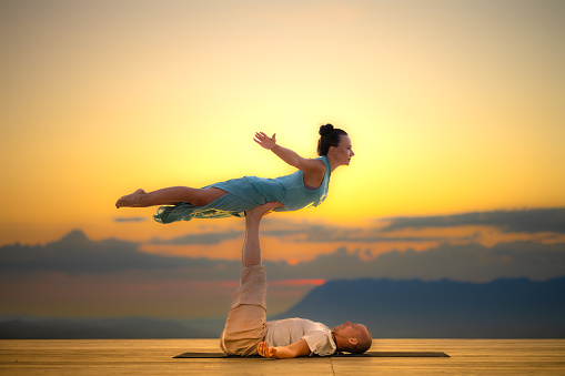 Side view of couple practising acroyoga yoga on deck during sunset.