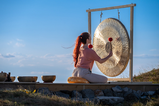 Young woman therapist playing gong against mountain during sunny day.
