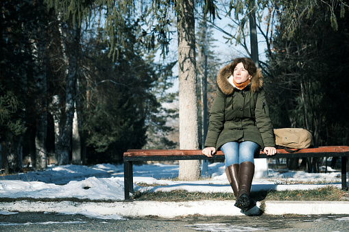 Mature woman is sitting on the bench in winter public park