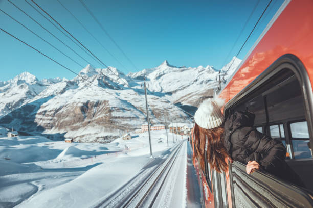 la viaggiatrice felice si affaccia dal finestrino viaggiando in treno nelle splendide montagne invernali, concetto di viaggio. - winter destination foto e immagini stock