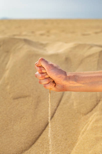 istock Sand slipping through fingers in-front of sand dunes 1448522765