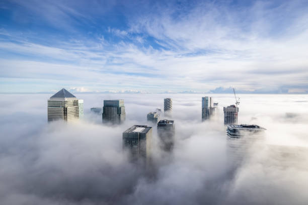The modern skyline of Canary Wharf, London, during a foggy day The modern skyline of Canary Wharf, London, during a foggy day with the tops of the skyscrapers looking out of the clouds sun above clouds stock pictures, royalty-free photos & images