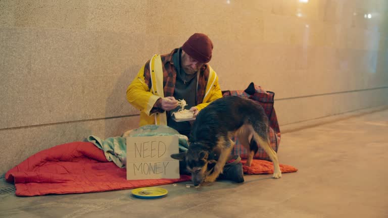 A homeless person is treating his dog while sitting on the ground