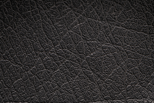 Black artificial or synthetic leather background with neat texture and copy space, colorful fabric sample with leather-like finish aimed for upholstery, fashion, sewing or footwear projects