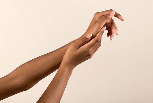 Crop anonymous African American female with French manicure touching hand gently on beige background