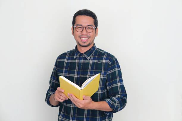 istock Adult Asian man smiling at camera while holding a book 1448524406