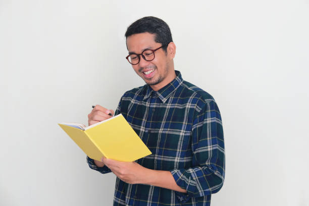 istock Adult Asian man smiling while writing something on a book 1448524408